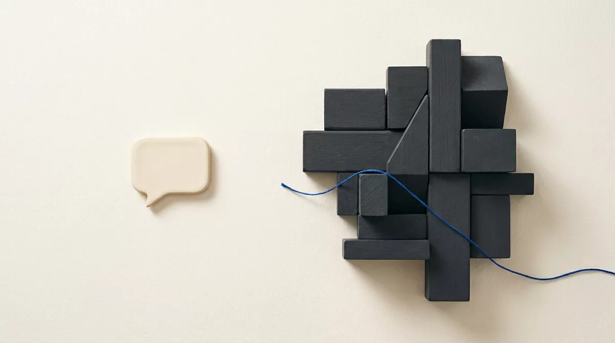 A small cream speech-bubble tile beside a larger structure of charcoal blocks, with a blue cord running into the structure.
