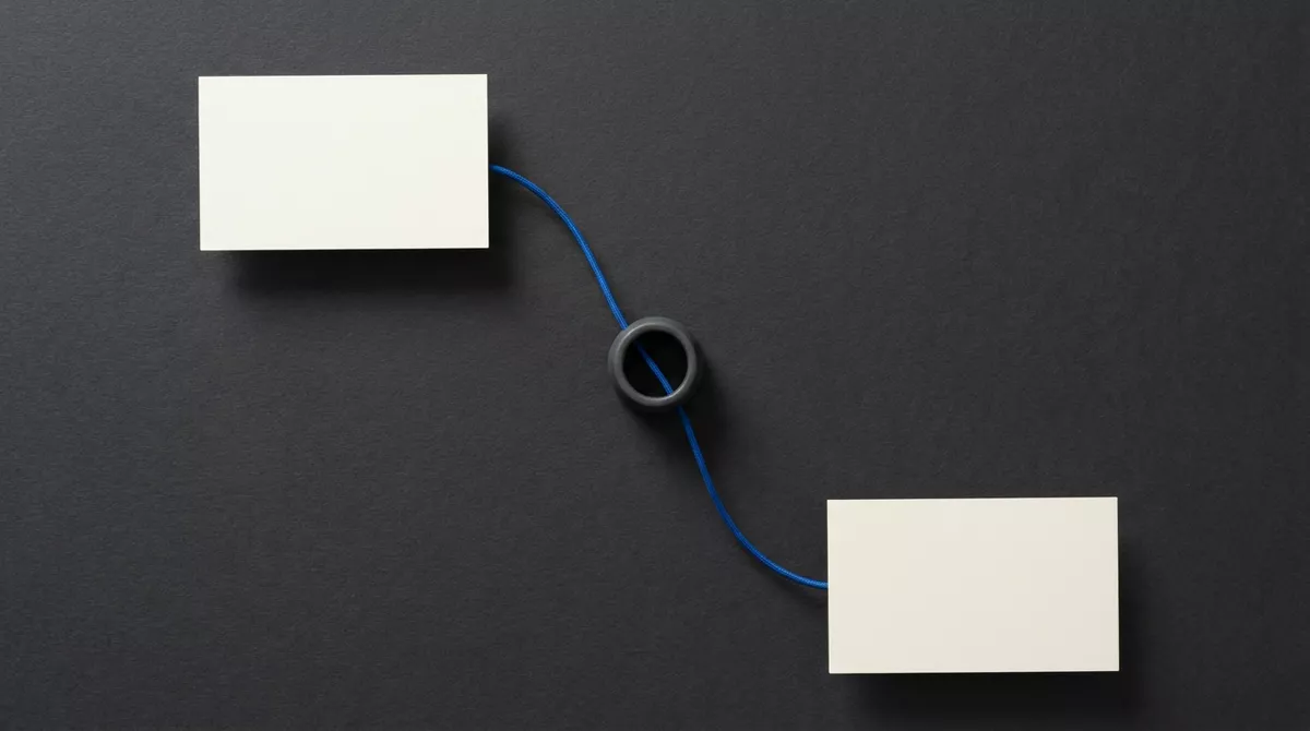 Two blank cream cards on charcoal paper, joined by a blue cord that passes through a charcoal ring between them.