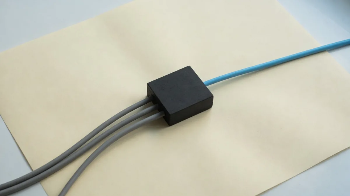 Three grey cables enter a charcoal block and one blue cord leaves it.