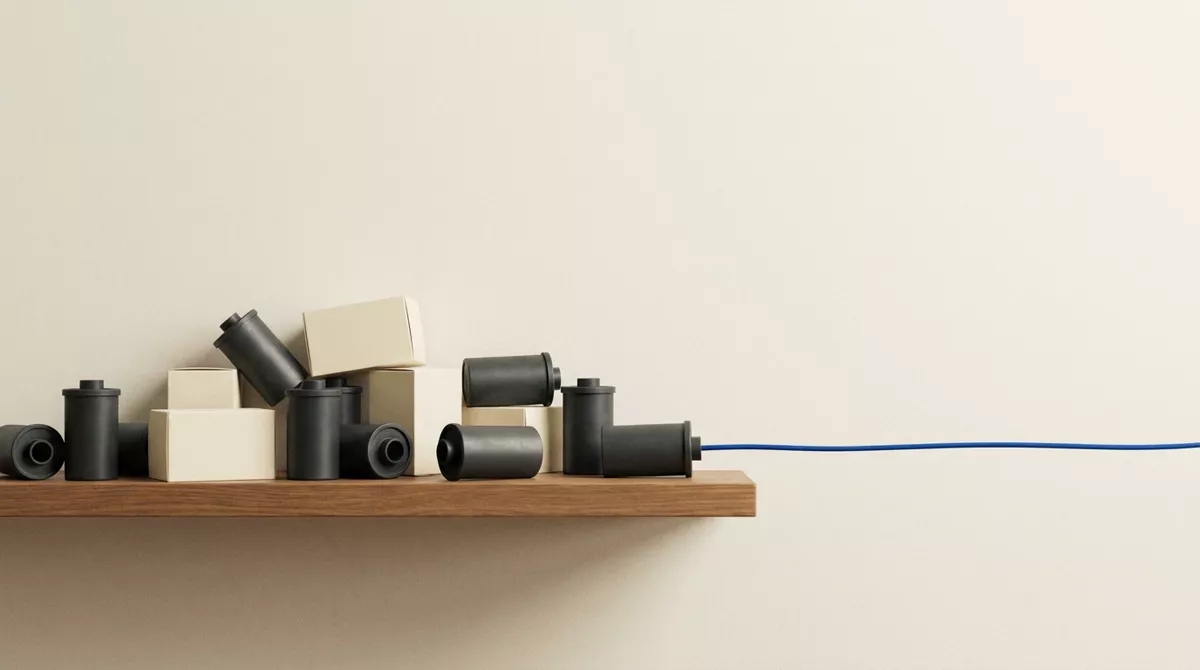 A low wooden shelf of charcoal film cans and cream boxes, with a blue cord running from one can off the edge of the frame.